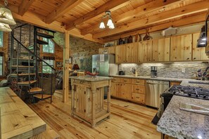 A rustic kitchen with wooden cabinets, a central island, a built-in stove, and a stone accent wall. - PICK'S RIVERSIDE RETREAT - 2 Bedroom plus Loft Riverside Retreat on the Upper Toccoa River (Blue Ridge)