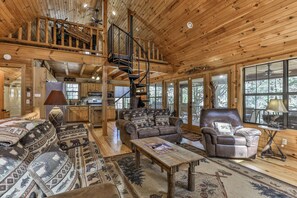 A spacious cabin interior with a loft bedroom, a dining area, and a living room furnished with leather sofas and a coffee table. - PICK'S RIVERSIDE RETREAT - 2 Bedroom plus Loft Riverside Retreat on the Upper Toccoa River (Blue Ridge)