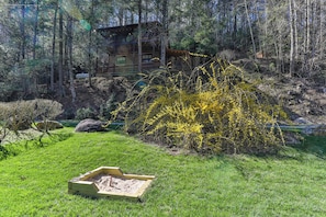 Une cabane en bois entourée d’une forêt, avec un petit jardin aménagé au premier plan.