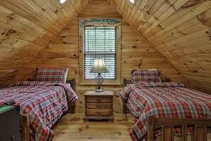 A cozy attic bedroom with two beds, a nightstand, a lamp, and a window with blinds. - PICK'S RIVERSIDE RETREAT - 2 Bedroom plus Loft Riverside Retreat on the Upper Toccoa River (Blue Ridge)