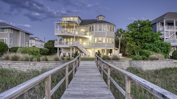A waterfront property with a wooden boardwalk leading to a multi-story building with balconies and a wrap-around porch. - RARE Oceanside 5BR Waterfront Home w/ pvt Dock! (Wrightsville Beach)
