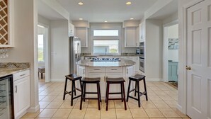 A modern kitchen with a central island, white cabinetry, and a large window. - RARE Oceanside 5BR Waterfront Home w/ pvt Dock! (Wrightsville Beach)