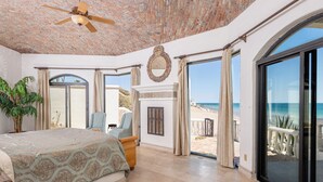 Une chambre spacieuse avec un grand lit, un ventilateur de plafond et une vue sur la plage, accessible par une porte-fenêtre coulissante.