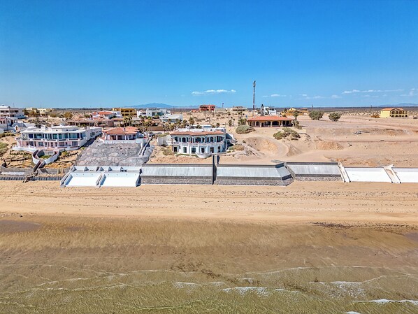 Zona costera con edificios modernos, incluyendo una casa grande con balcón y una construcción más pequeña con techo rojo.