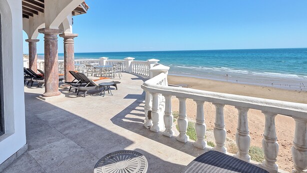 Une terrasse au bord de la plage, dotée de chaises longues et de tables, avec vue sur l’océan.