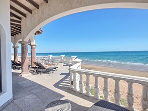 Un patio frente a la playa con sillones y mesas, con vista al océano.