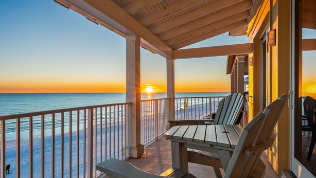 A covered outdoor area with a view of the sunset over the ocean, featuring a table and chairs.