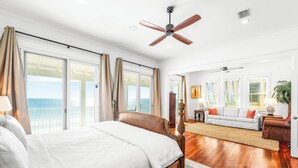 A spacious bedroom with a large bed, a ceiling fan, and a view of the ocean through large windows.