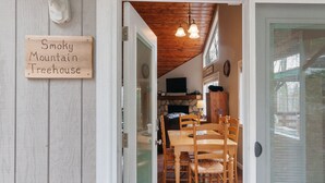A wooden door with a sign reading "Smoky Mountain Treehouse." Inside, there is a dining area with a wooden table and chairs. - 2 Master Suites - Hot Tub - Porch - Fire Pit - Wi-Fi - Clean - Cozy - 5 Stars! (Maggie Valley)