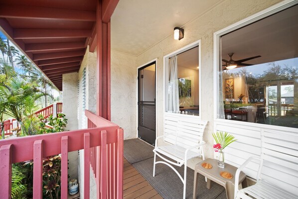 A covered outdoor area with a wooden deck, white chairs, and a table with a vase of flowers.