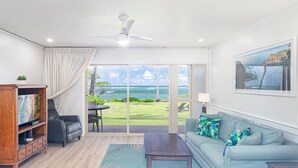 Un salon avec vue sur l’océan, un ventilateur de plafond, un canapé, une table basse et un meuble en bois.