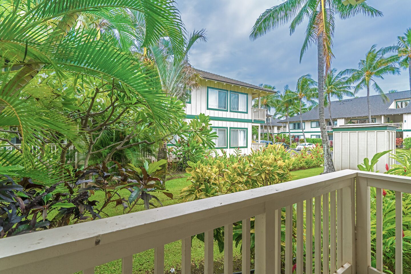 A hotel with a white exterior, green trim, and a balcony with a wooden railing.