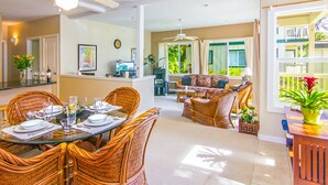 Ein Essbereich mit Korbmöbeln und einem Glastisch, ein Wohnzimmer mit Sofa und Sesseln sowie ein Balkon mit Pflanzen.