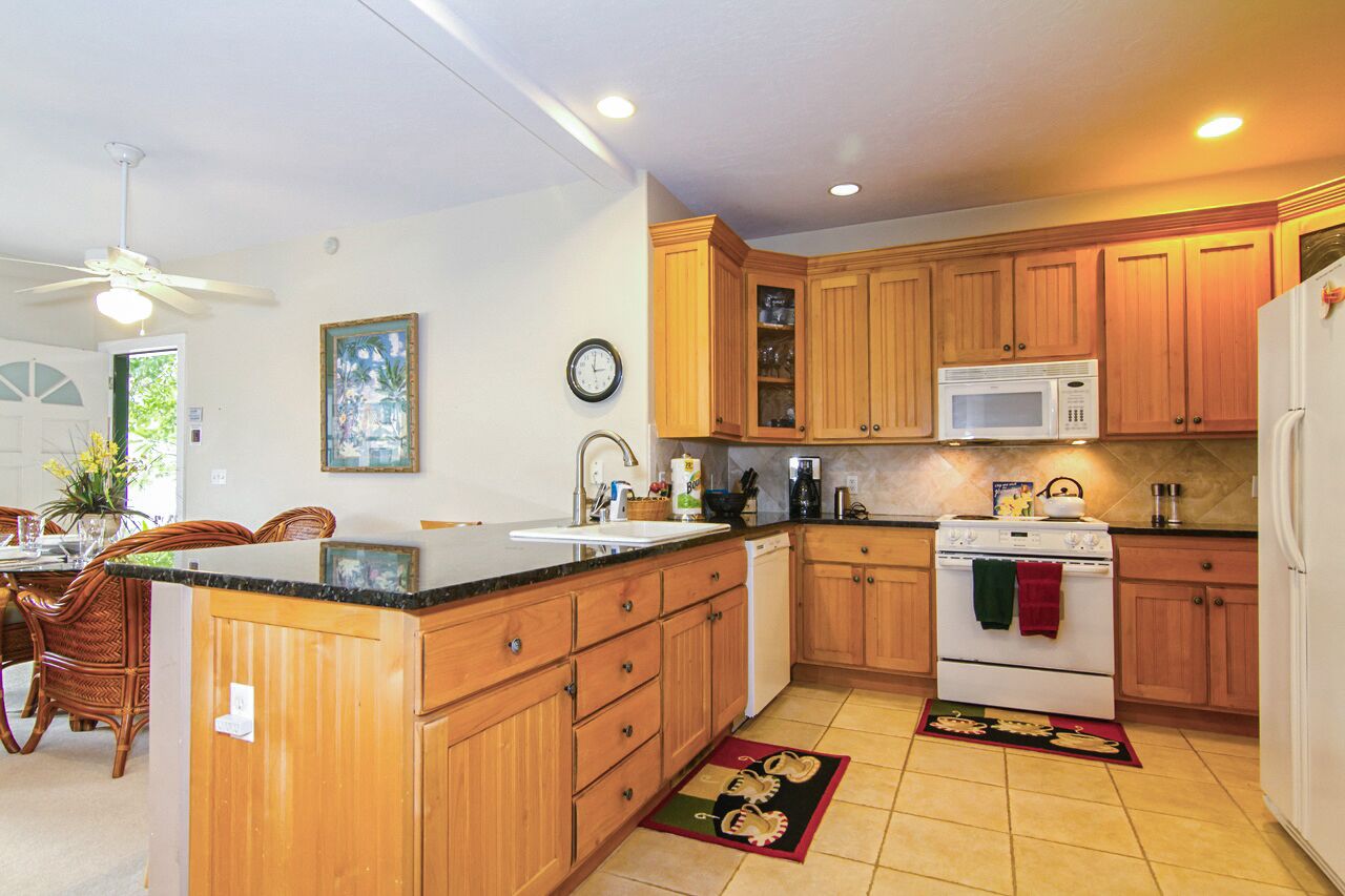 A kitchen with wooden cabinets, a white stove, a microwave, and a dining area with wicker chairs and a table.