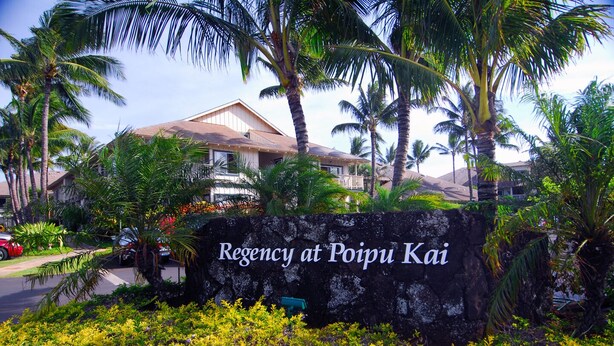 Schild für das Regency in Poipu Kai mit Steinmauer und tropischen Pflanzen.
