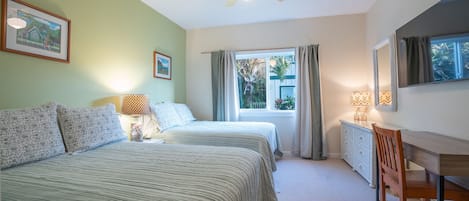 Un dormitorio con dos camas, ventilador de techo, ventana con cortinas, escritorio con silla y cómoda.