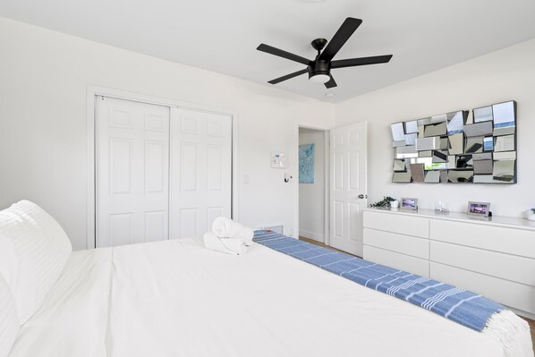 A bedroom with a bed, a ceiling fan, a dresser, and a mirror on the wall.