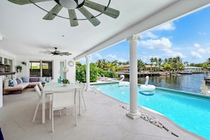Un espace piscine comprenant une table et des chaises, un ventilateur de plafond et une vue sur une marina avec des bateaux.