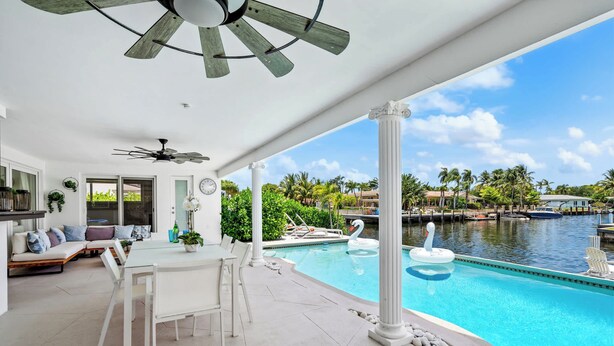 A pool area with a dining table and chairs, a ceiling fan, and a view of a marina with boats.