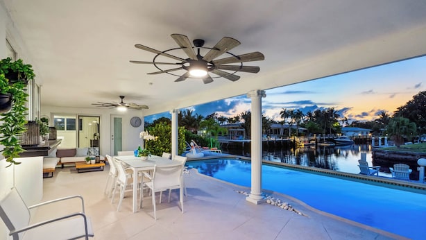 A covered outdoor area with a pool, seating, and ceiling fans.