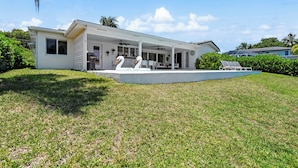 A modern house with a covered patio, a swimming pool, and two swan statues.