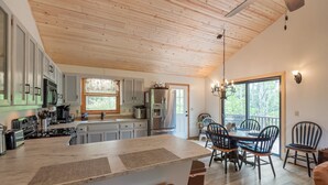 Une cuisine spacieuse avec un plafond en bois, un grand îlot central et un coin repas comprenant des chaises et une table.