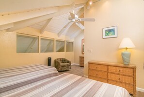 Un dormitorio con dos camas, un ventilador de techo, un aparador de mimbre y una lámpara.
