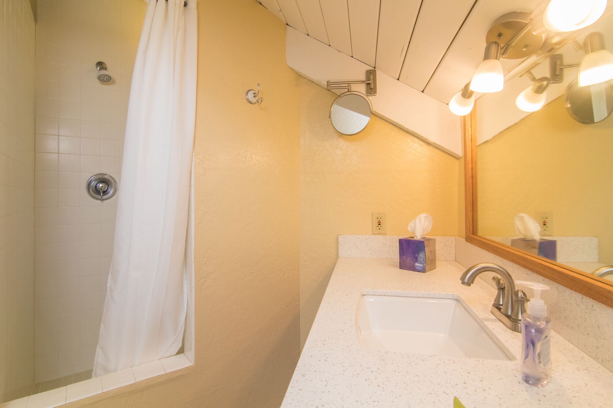 A bathroom with a shower, a sink with a mirror, and a towel dispenser.