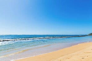 Uma praia com águas azul-claras, areal arenoso e um paredão rochoso.