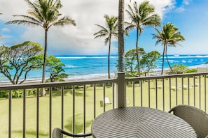 Relax on the balcony surrounded by lush greenery and palm trees, with a view of the ocean.