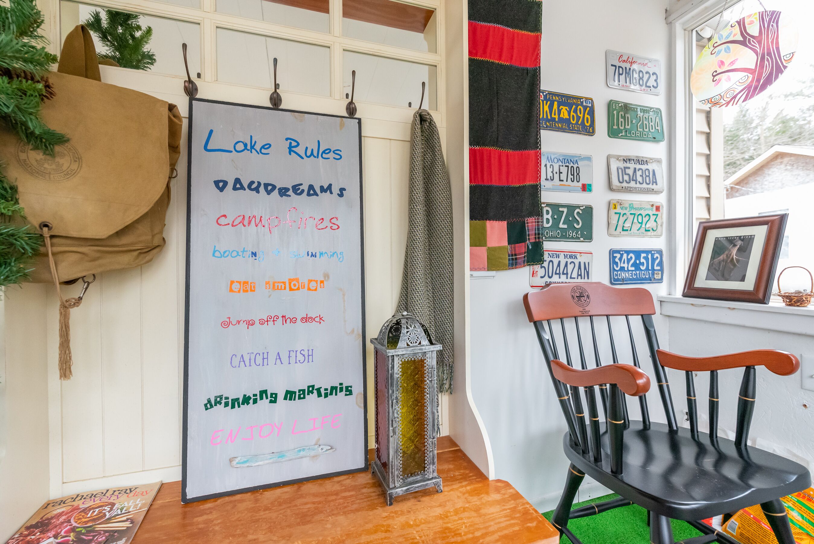 A room with a whiteboard listing outdoor activities, a wooden chair, a small lantern, and a window with a view of trees.