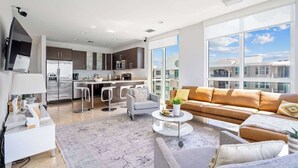 A modern living room with a sofa, coffee table, and a view of the kitchen. - Hemingway Penthouse South - Two Blocks from the Beach! (Deerfield Beach)