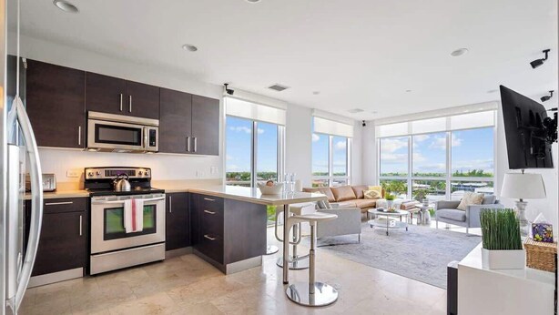 A modern kitchen with dark cabinets, stainless steel appliances, and a large island. - Hemingway Penthouse South - Two Blocks from the Beach! (Deerfield Beach)