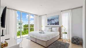 A modern bedroom with a large bed, a desk, and a view of the city. - Hemingway Penthouse South - Two Blocks from the Beach! (Deerfield Beach)
