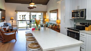 A modern kitchen with white cabinetry, a central island, and a dining area with wicker chairs and a sofa.