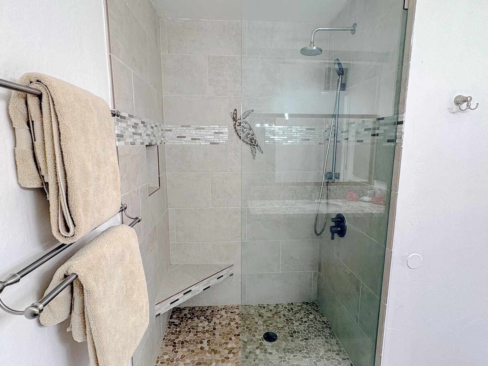 A glass-enclosed shower area with a tiled floor, a towel rack with a towel, and a showerhead.