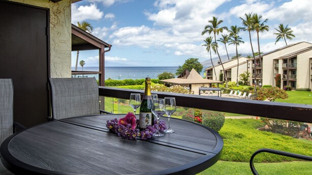 A balcony with a table set for two, a bottle of wine, and purple flowers.