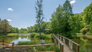 A wooden bridge leading to a gazebo by a lake surrounded by lush greenery.