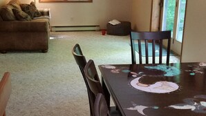 A dining area with a large table, chairs, a sofa, a lamp, and a painting on the wall.