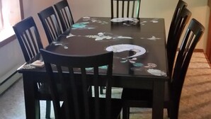 A dining room with a round table, six chairs, a chandelier, and a wall clock.
