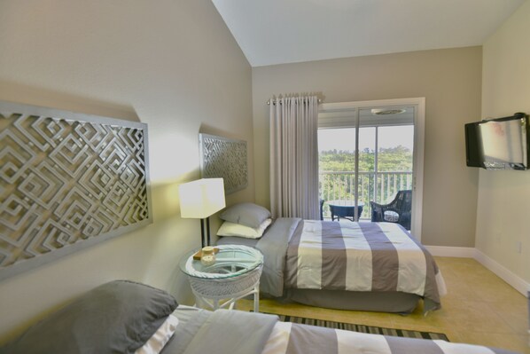 Habitación de hotel con dos camas, televisor, ventana con cortinas y balcón con sillas.