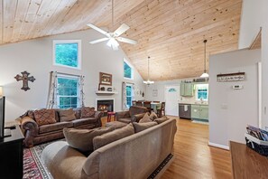 A spacious living room with a fireplace, a dining area, and a kitchen with green cabinets. - Jackson's Ridge Overlooking New River | Covered Hot Tub | Dog-Friendly (West Jefferson)