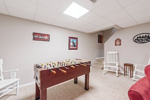 A room with a foosball table, a white chair, and a staircase.