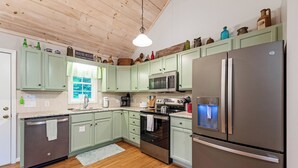 Une cuisine avec des meubles de couleur vert clair, des appareils électroménagers en acier inoxydable et un plafond en bois.