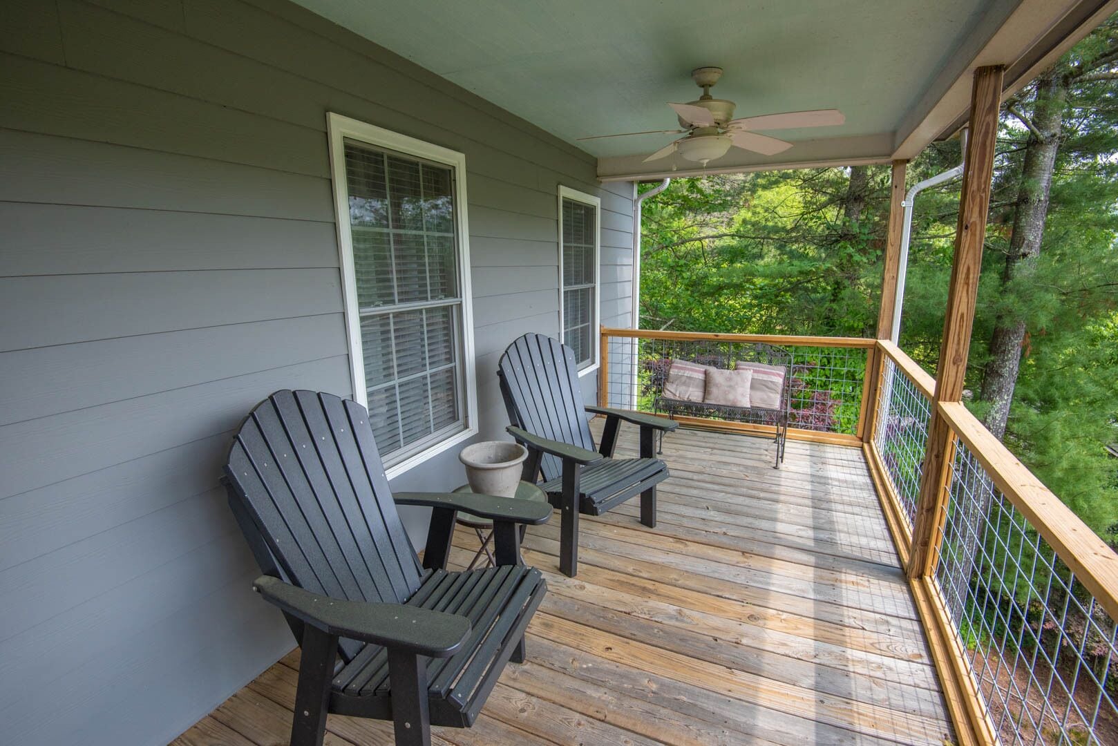 A wooden deck with two Adirondack chairs and a small table, overlooking a lush green forest.