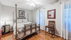 Une chambre à coucher avec un lit à baldaquin, un ventilateur de plafond, une table de chevet, une chaise et une fenêtre avec des rideaux.