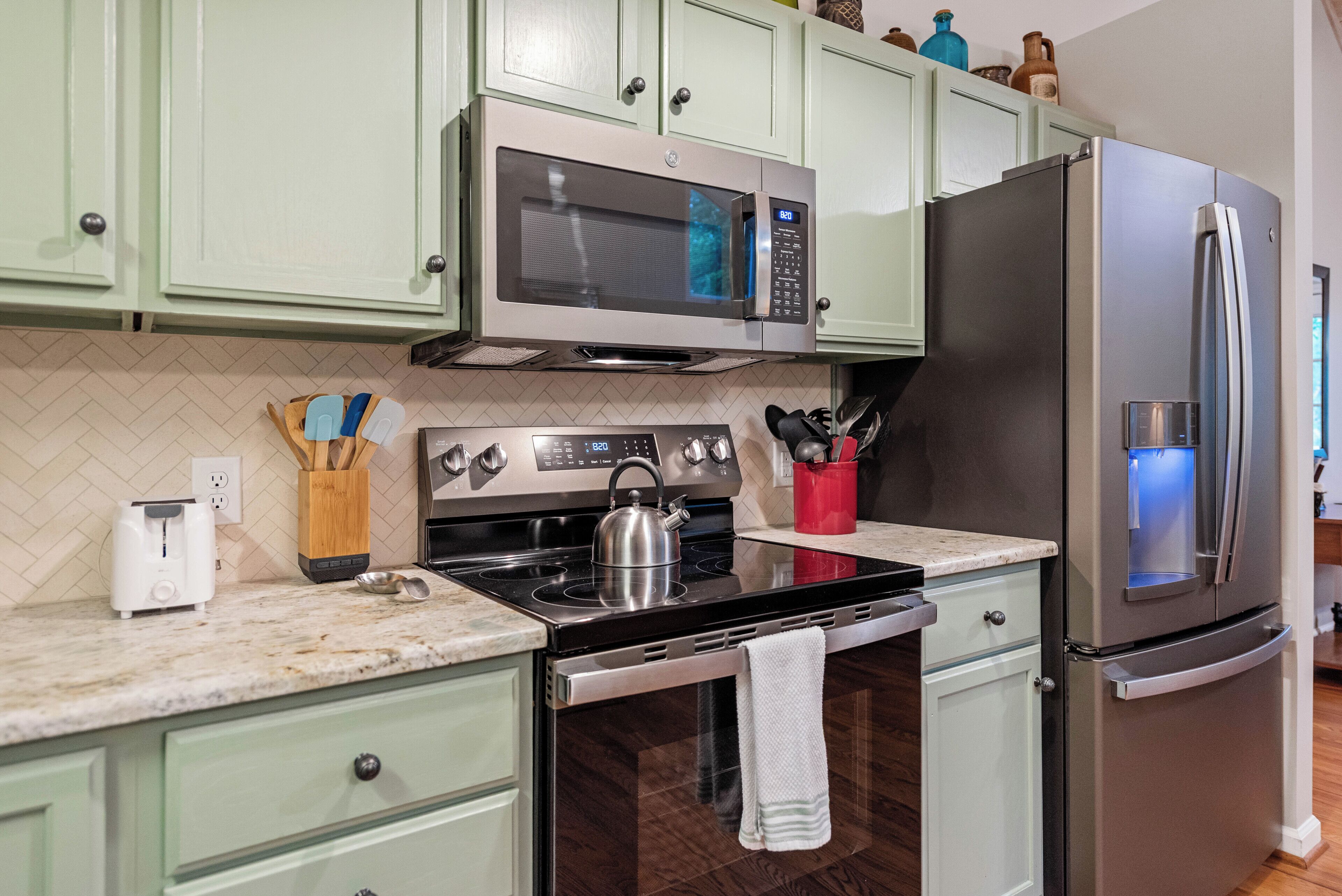 A kitchen with light green cabinets, a stainless steel refrigerator, a microwave, a stove, and a toaster.