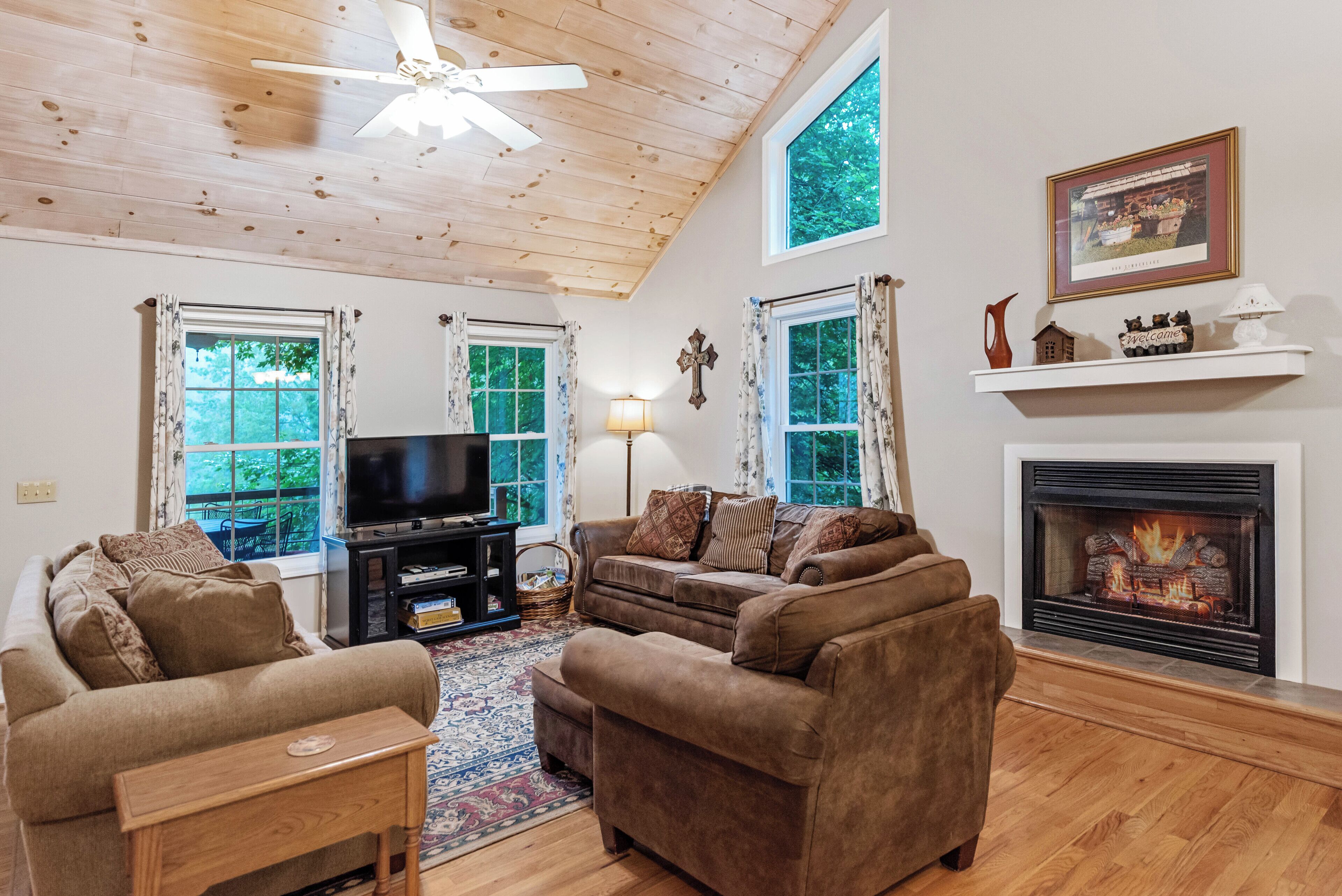 A living room with a fireplace, a television, and a ceiling fan.