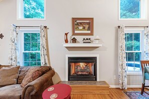 A living room with a fireplace, a sofa, a red table, and a window with curtains.