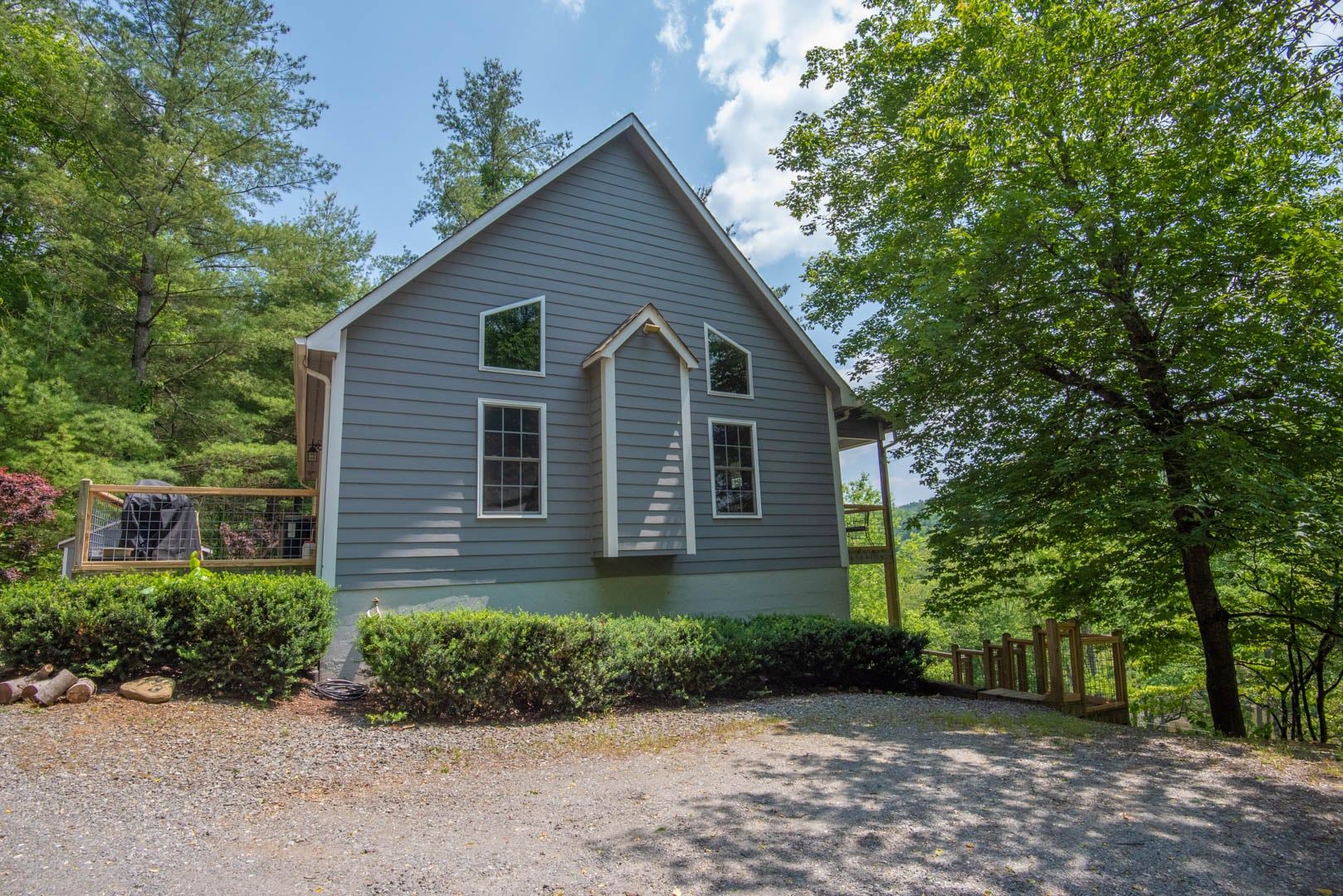 A two-story house with a gabled roof, surrounded by a gravel driveway and dense greenery.